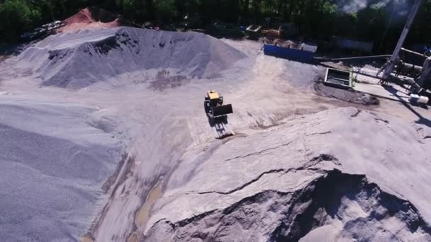 花崗岩の採石場の黄色いローダー掘削機 瓦礫の大規模な山 アスファルト工場 花崗岩採石場の粉砕機上空の空中飛行 — ストック動画