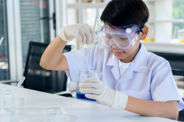 Asian boy wearing protection eyeglasses use a glass bulb drop of dark blue and looking to blue liquid in chemistry lesson at laboratory