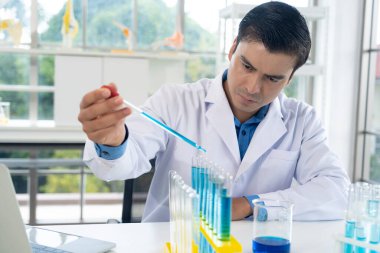 Handsome researcher man in white coat drop blue liquid into glass tube at laboratory while working in the laboratory, copy space