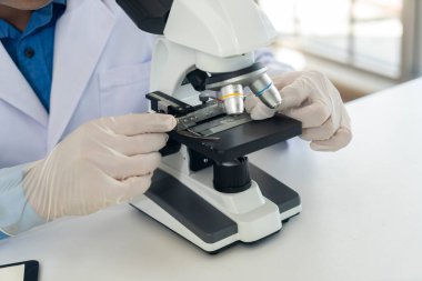 Young scientist man in lap coat and gloves working with microscope during researching chemistry at laboratory, copy space