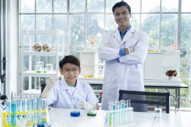 Portrait of Young man teacher and little boy wearing lap coat in chemistry class at laboratory, smile and looking to camera, copy space
