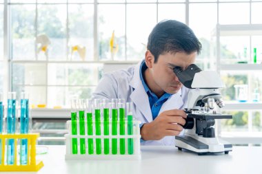 Young male researcher in lab coat looking through microscope with thoughtfully while working in the laboratory, copy space