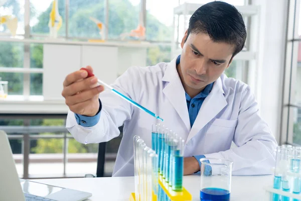 Handsome researcher man in white coat drop blue liquid into glass tube at laboratory while working in the laboratory, copy space