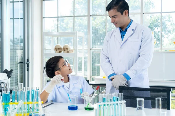 Young man teacher and little boy wearing lap coat in chemistry class at laboratory, smile and looking together, copy space