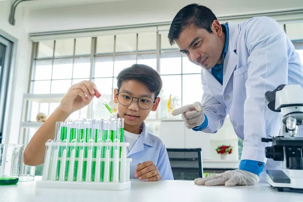 Young man teacher with little boy, He use glass bulb to suck and drop liquid into glass tube during teaching chemistry at laboratory