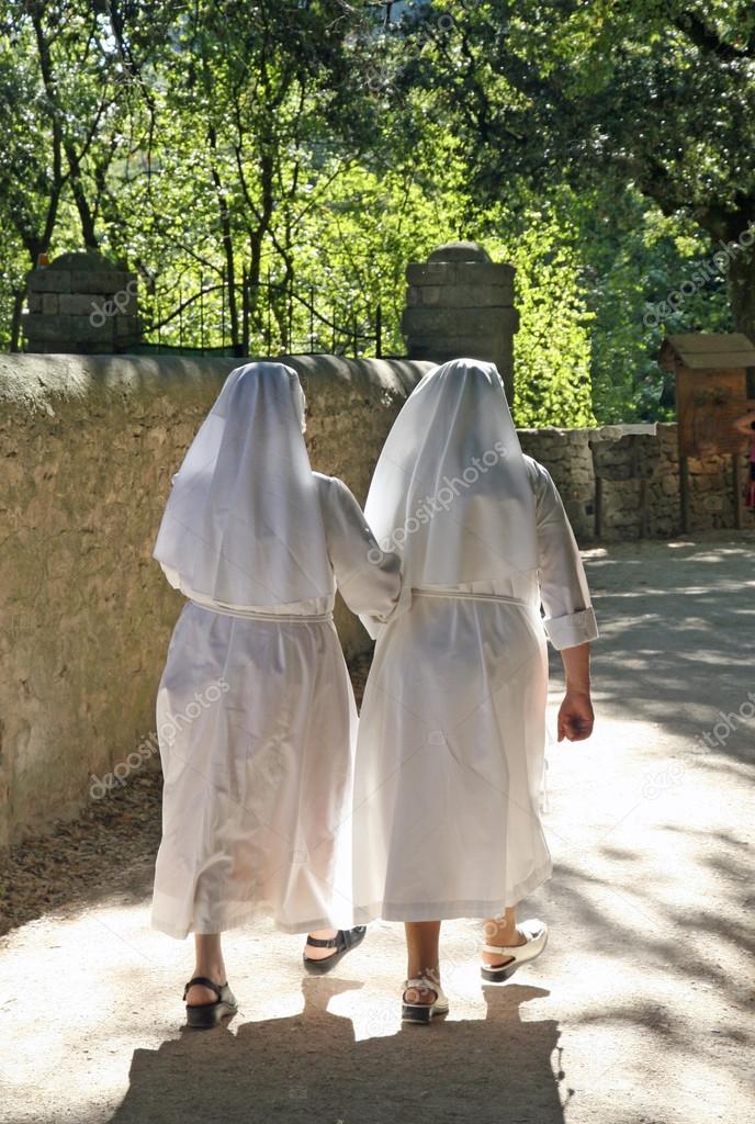 Two nuns dressed in white walk along the path