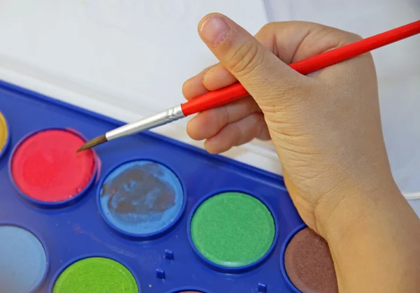 Hand van een jong meisje met een borstel en aquarellen — Stockfoto