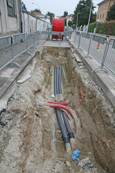 Road excavation at a construction site at conduits for the layin — Stock Photo, Image