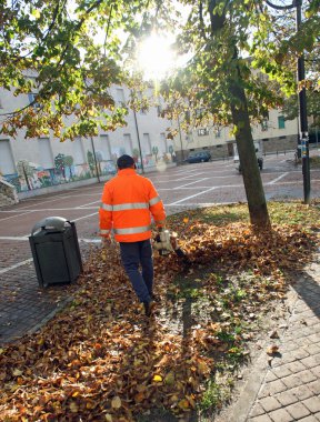 kurutulmuş yaprakları esen ise turuncu ceket ile sokak süpürme aracı
