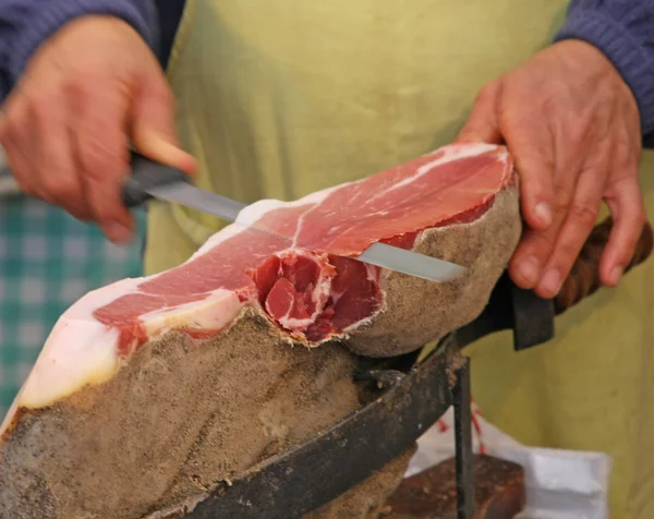 Butcher's hand while fast cuts a piece of prosciutto crudo — Stock Photo, Image