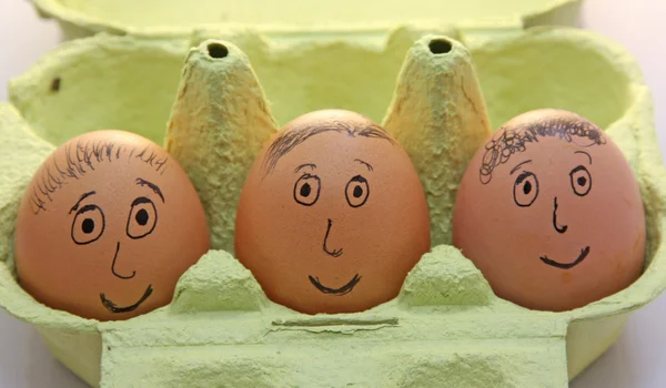 Tre uova con occhi e naso sorridenti e bocca e capelli — Foto Stock