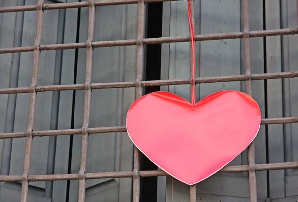 Coração vermelho pendurado na grade de uma janela fora de um edifício em — Fotografia de Stock