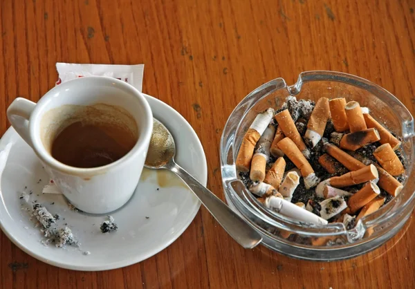 Taza de café expreso y cenicero lleno de colillas de cigarrillos — Foto de Stock