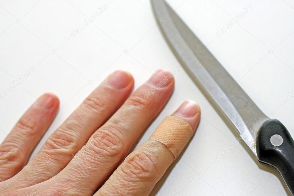 hand with finger with a band aid and the sharp blade of the knif