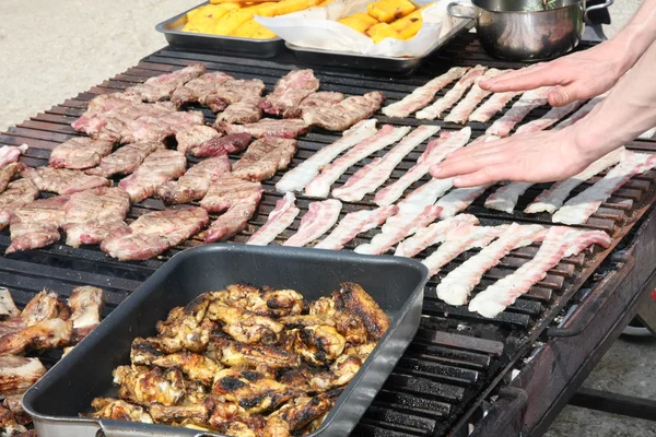 Mãos de cozinheiro enquanto cozinha em uma grade gigante de um churrasco ao ar livre — Fotografia de Stock