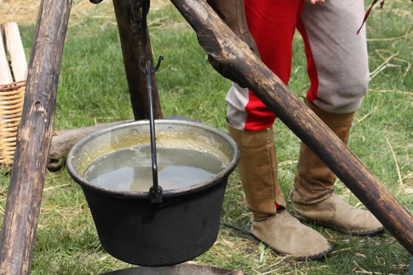 Antigua olla medieval con agua en el fuego y trípodes para suppo —  Fotos de Stock