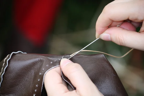 Mulher enquanto costura um vestido de couro com agulha e fio — Fotografia de Stock