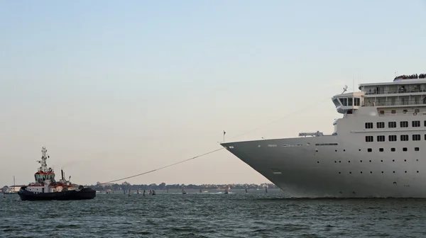 Mächtiger Schlepper, während er das große Kreuzfahrtschiff aus dem Hafen manövriert. — Stockfoto