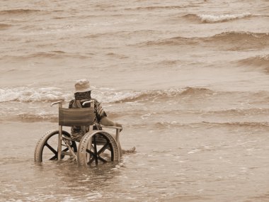 elderly woman in a wheelchair in the sea with sepia color clipart