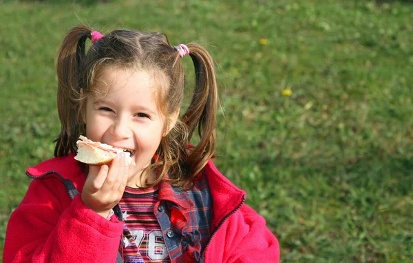 Молодая девушка во время еды сэндвича, улыбаясь — стоковое фото