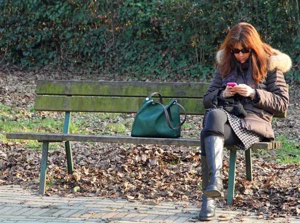 Mulher no banco enquanto estiver usando seu telefone celular — Fotografia de Stock