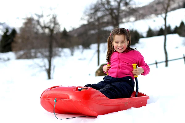 Całkiem mała dziewczynka gra na śniegu z zabawki bob — Zdjęcie stockowe