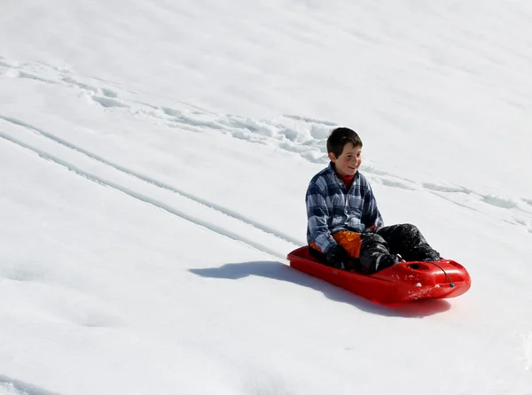 Kid down nedstigningen med röda bob på vit snö — Stockfoto