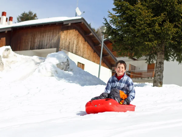 Ung pojke ner nedstigningen med röda bob på vit snö — Stockfoto