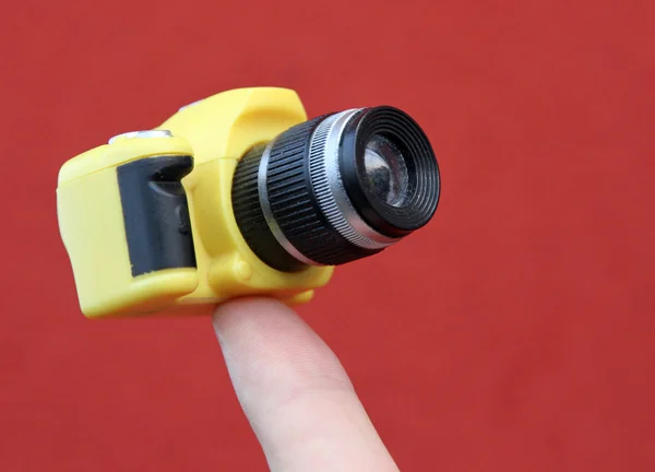 Küçük, sarı, askıya alınan bir kamera tutarak işaret parmağı — Stok fotoğraf