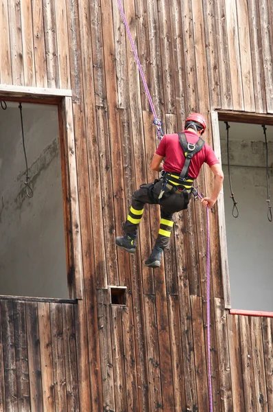 Brandweerman klimmer naar beneden in de muur van het huis in abseilen — Stockfoto