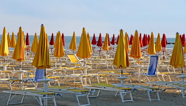 Guarda-chuvas fechados e espreguiçadeiras na praia ao pôr do sol na se — Fotografia de Stock