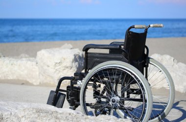 wheelchair on the rocks of the blue sea in summer clipart