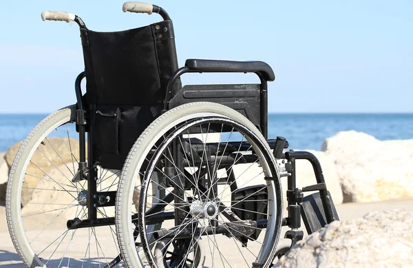 Черная инвалидная коляска на скалах моря — стоковое фото