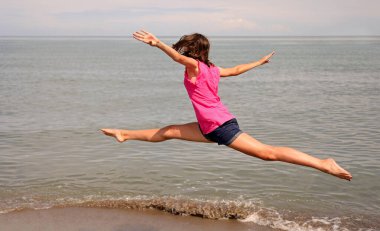Kafkasyalı kız zor ritmik jimnastik egzersizleri yapıyor ve kumsalda havada bölünme var.
