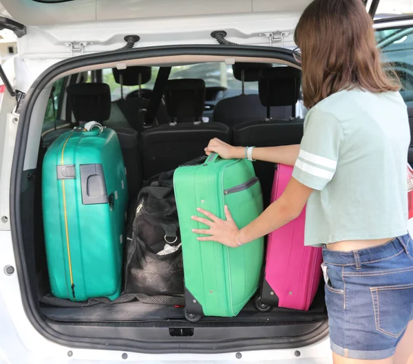 若い女の子が長い旅の前に車のトランクにスーツケースをロードしながら — ストック写真