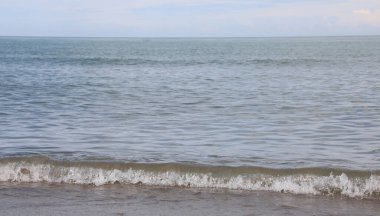 Sakin denizin basit arka planında, yazın kumsalın kumlu sahillerinde insanlar olmadan alçak dalgalar...