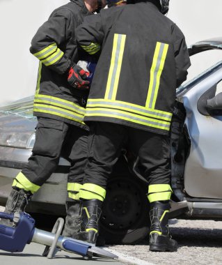 İki üniformalı itfaiyeci trafik kazasından sonra güçlü bir hidrolik makasla yolcu vagonunu açıyor.