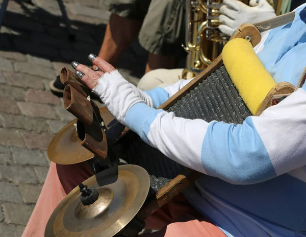 elderly player from Eastern Europe with a particular handmade musical instrument with sound cymbals and a board where you can drag your fingers protected by thimbles to emit sounds and rhythms