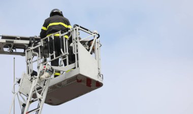 Acil bir durum ve arka planda gökyüzü varken merdiven kamyonunu kullanarak yaralı kişiyi kurtaran cesur itfaiyeci.