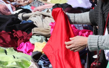 Çarşıda kırmızı elbise deneyen kadınların ellerinde satılık bir sürü kıyafet var.