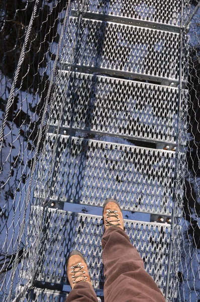 legs of man that walks on the very long  suspension bridge in stainless steel in winter