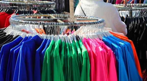 屋外市場の流行の衣料品店のハンガーに掛けられた複数の色の服 — ストック写真