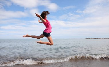 Deniz kenarındaki atletik kız yazın kısa şortla yüksek atlama yaptıran ritmik jimnastik egzersizleri yapıyor.