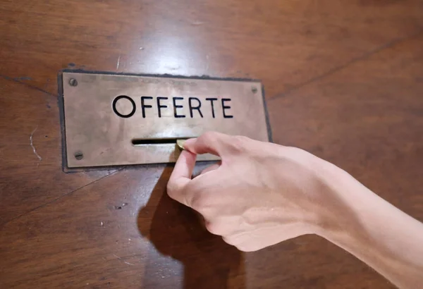 hand of boy putting a coin into the offer box with the inscription OFFERTE the means offer in Italian language