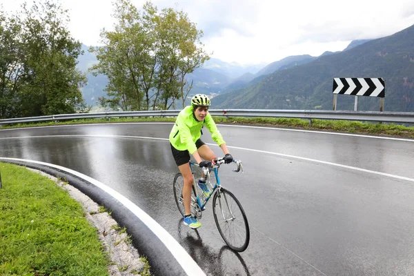 young boy cyclist with racing bicycle while making a curve on wet road during sports training while raining