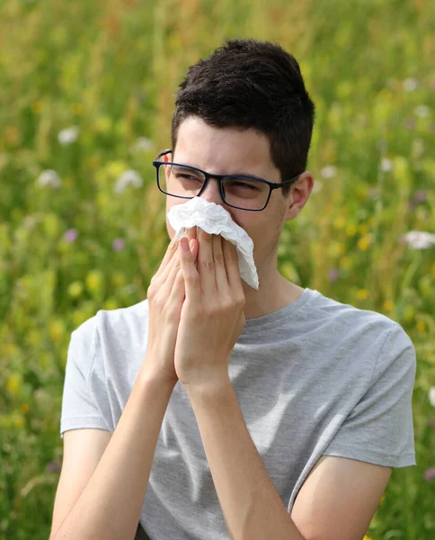 組織でくしゃみをする眼鏡をかけた少年は草にアレルギーがあるので — ストック写真