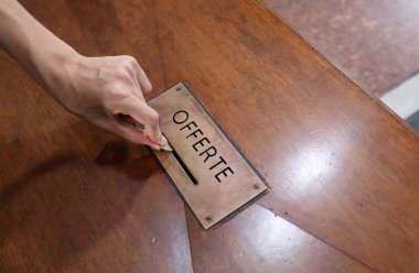 hand of boy who puts coin on the box with text OFFERTE that means OFFERS in Italian Language in the church clipart