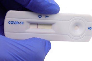 Mavi lateks eldivenli el covid-19 testi için tıbbi cihazı tutuyor. Negatif sonuç veriyor ve beyaz arka planda kontrol çizgisi var.