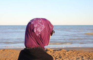 Kafasında siyah peçeli bir kadın ve sahilde tekneyi bekleyen tipik Arap kıyafetleri.