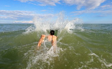 Genç çocuk deniz suyunun ortasında büyük bir dalış yapar ve ayaklarının spreyden çıktığını görürsünüz.